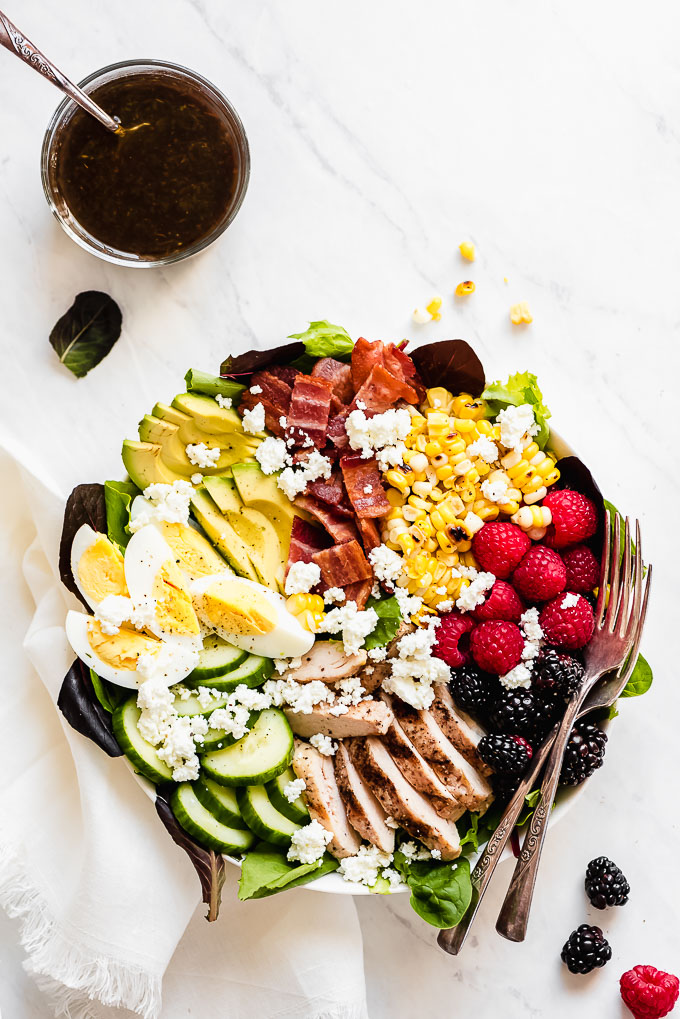 Bowl of Cobb Salad on a marble surface with forks on the side of the bowl.