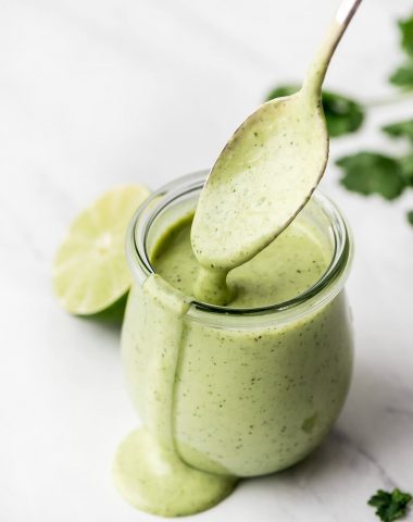 A jar of Cilantro Lime Dressing with a spooning being lifted out and dressing dripping back into the jar.