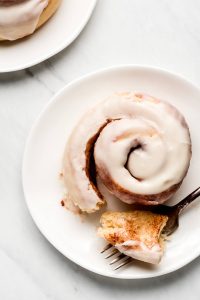 Frosted Cinnamon Roll partially unwound with a piece cut off and on a fork.